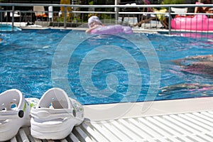 Pool and Slippers on the side. A girl swims in the background.