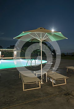 Pool, sunbeds and umbrellas at night