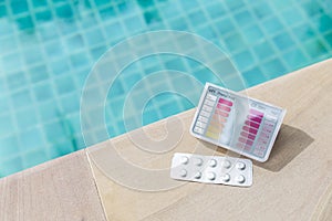 Pool tester test kit and tablets on swimming pool edge, summer outdoor day light
