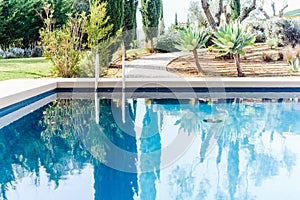 Pool with turquoise water and white sun loungers in a pine forest