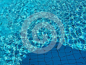 Pool water. Blue and turquoise pattern on surface. Blue colored pool water with bright and dark parts and sun reflections