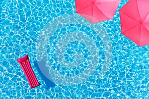 Pool water pink matrass and umbrella from above