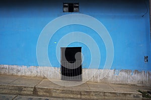 poor and abandoned house with dirty adobe wall dirth with closed wooden door street and sidew