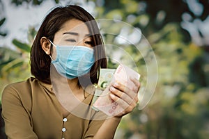 Poor Asian woman wearing protective mask hand holding less money having problem with low income