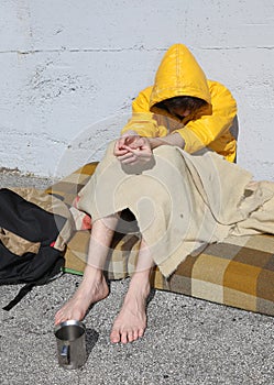 Poor barefoot homeless man in a yellow hood asks for charity fro