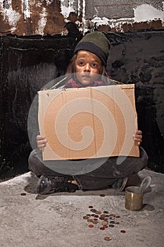 Poor beggar boy on the street with a cardboard sign