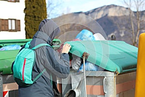 Poor boy with a backpack on his back searching in the rubbish bi