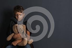 Poor boy sitting with toy rabbit on dark background.