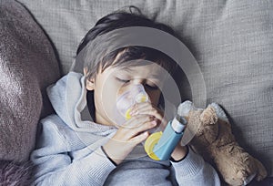 Poor boy tired from chest coughing holding inhaler mask, Child closing his eyes while using the volumtic for breathing treatment,