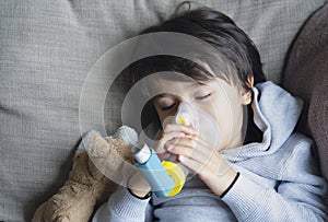 Poor boy tired from chest coughing holding inhaler mask, Child falling a sleep while using the volumtic for breathing treatment,