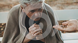 Poor elder homeless man receiving coins from woman