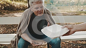 Poor elderly homeless man counting left coins in the park and receiving charity meal