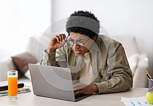 Poor eyesight. Black teenager in glasses squinting his eyes while using laptop computer for online education at home photo