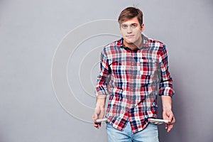 Poor handsome young man in checkered shirt showing empty pockets
