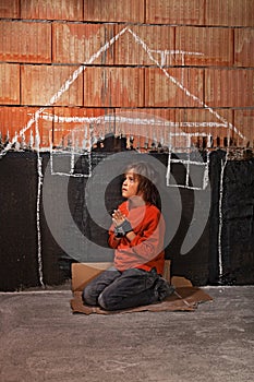 Poor homeless beggar boy praying for a shelter concept