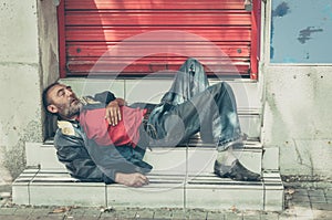 Poor homeless man or refugee sleeping on the stairs on the street, social documentary concept photo