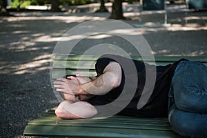 Poor homeless man sleeping on the wooden bench at park