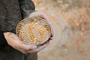 Poor homeless woman with bowl of wheat outdoors