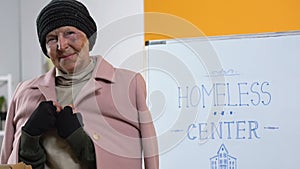 Poor homeless woman in donated warm clothing looking to camera in support center