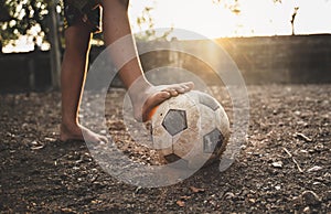 Poor kid playing old soccer or football on ground with glowing sunlight background and hope concept