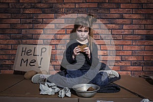 Poor little girl with bread and HELP ME sign on floor near wall