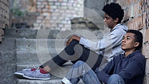 Poor lonely teenagers looking away sitting abandoned building, difficulties