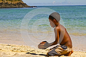 Poor malagasy boy breaking coconuts on the beach
