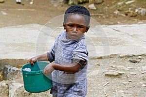 Poor malagasy boy carrying plastic water bucket