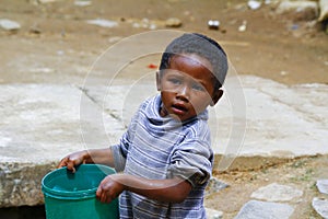 Poor malagasy boy carrying plastic water bucket