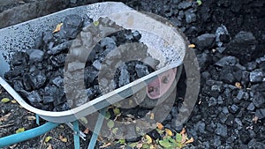 A poor man loads natural coal in a truck with a shovel.