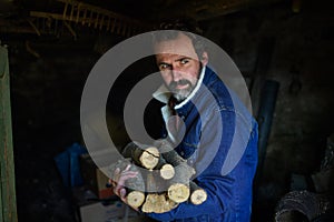 Portrait of poor mature man holding firewood at home, looking at camera, poverty concept.