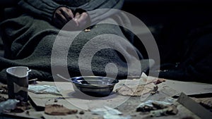 Poor person in dirty cloth sitting front of bowl, living on street, homelessness