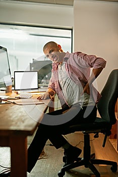 Poor posture can trigger all sorts of pain. a young designer experiencing back pain while working late at his desk.