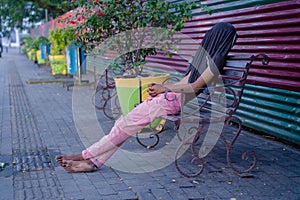 Poor tired depressed hungry homeless man or refugee sleeping on the wooden bench on the urban street in the city