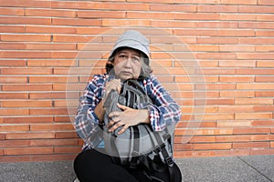 Poor tired stressed depressed elderly Asian woman homeless sitting on the street in the shadow of the building and begging for