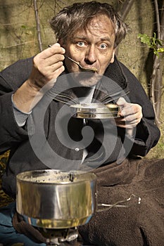 Poor unemployed man on backstreet yard place eating lentil soup