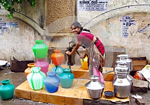 Poor young Indian woman in a sari with colorful pots near the water source