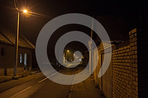 Poorly lit dark street in a rural countryside environment, surrounded by residential houses and orange public lighting