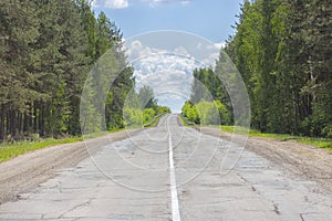 A poorly-paved rural two-lane road, deciduous forest, cloudy sky, highway to the horizon