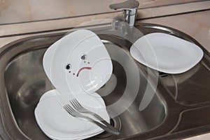 Poorly washed dishes in kitchen sink. White plate with sad emotion. Kitchen faucet