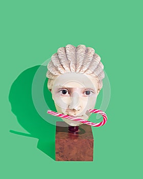 Pop art minimal concept. Christmas and New Year creative card. Statue head with Christmas candy cane in mouth and collage