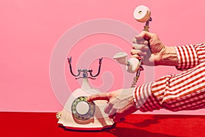 Pop art photography. Retro objects, gadgets. Female hand holding handset of vintage phone isolated on pink and red