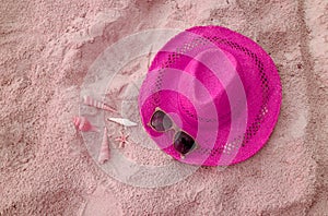 Pop art shocking pink straw hat with sunglasses and little seashells on pastel pink sandy beach