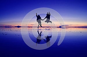 Pop art styled royal and coral pink colored of happy couple silhouette jumping on the MIRROR EFFECT of Uyuni Salt Flats in Bolivia