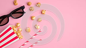 Pop corn in striped red and white cardboard box, 3d glasses, drink straws on pink table top view. Online cinema, watching movie