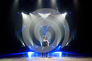 Pop musician with microphone singing a song on the stage in blue light background.