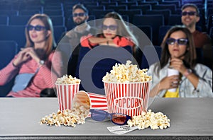 Popcorn, 3D glasses on table and people in cinema hall