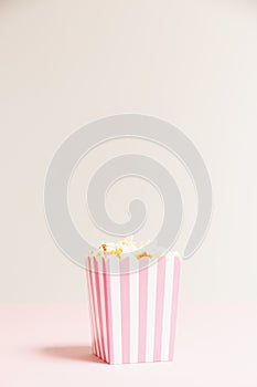 Popcorn bag with white and pink stripes at the light neutral backdrop. Empty minimalistic background. Romantic movie