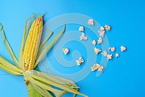 Popcorn in a bowl with corn cobs on blue background, top view. Copyspace.