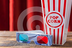 Popcorn In Classic Cinema Serving Box And 3D Glasses For Wathcing Movies On Wood Background With Red Theater Curtains.